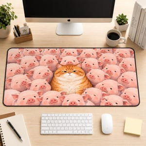 May include: A rectangular desk mat featuring a central illustration of a grumpy orange tabby cat surrounded by a large group of cheerful pink piglets. The mat has a black border and is positioned on a wooden desk surface in front of a computer.