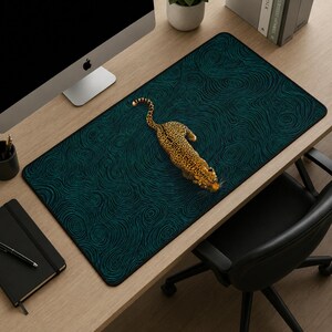 May include: A rectangular desk mat featuring a dark teal background with a swirling, topographic-style line pattern. Centered on the mat is a detailed, top-down illustration of a spotted leopard with golden-yellow fur and black rosettes.
