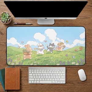 May include: A rectangular desk mat featuring a whimsical illustration of a bunny and cats frolicking in a field. The design includes a blue sky, green hills, flowers, and butterflies. A keyboard, mouse, and computer are visible.