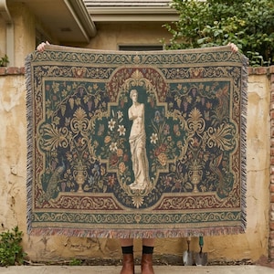 May include: Woven tapestry blanket featuring a classical statue, floral and peacock motifs in shades of green, brown, and gold. The blanket has a fringed edge and a detailed, ornate design. The artwork is reminiscent of classical art.