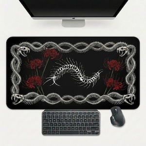 May include: Black rectangular mouse mat with a white snake skeleton border and snake heads. Red flowers and a white spine graphic are in the centre. A keyboard and mouse are below.