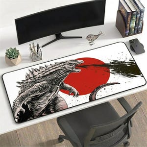 Puede incluir: Alfombrilla de ratón rectangular blanca con borde negro, que muestra una detallada ilustración en blanco y negro de Godzilla lanzando fuego frente a un sol rojo. La imagen forma parte de una configuración de escritorio.