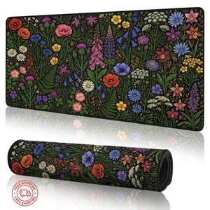 May include: A black desk mat featuring a vibrant floral design with red poppies, bluebells, and various wildflowers. The mat is rectangular and rolled up, showcasing the full pattern. The design includes green foliage and a black border.