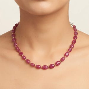 May include: A necklace featuring a single strand of smooth, oval-shaped, deep pinkish-red gemstone beads. The beads are arranged in a continuous pattern, separated by small, round, metallic gold-toned spacer beads along the entire length.