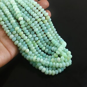 May include: A strand of smooth, round, pale mint green gemstone beads. The beads are uniform in shape and size, featuring a soft, translucent quality with subtle variations in color intensity throughout the entire length of the strand.