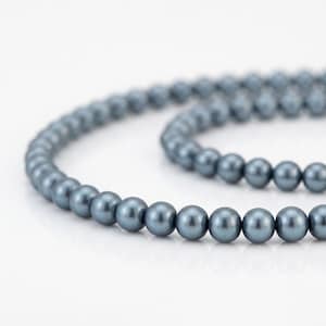 Puede incluir: Un collar de cuentas redondas y lisas de color azul pizarra, dispuestas en una formación curva y superpuesta. Cada cuenta presenta un acabado lustroso y uniforme que refleja la luz a lo largo de toda la longitud del accesorio.