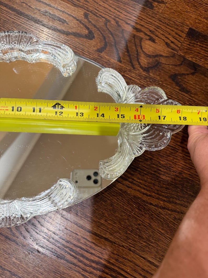 May include: An oval mirrored vanity tray with clear, textured glass handles featuring a fan-like pattern. A yellow measuring tape is placed across the tray, indicating a width of approximately 19 cm between the two glass handles.