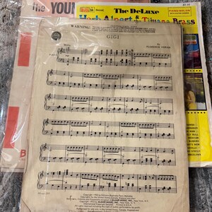 May include: Sheet music for "Gigi" by Florence Veran, featuring piano solos with guitar chords. The cover is yellowed with age, and the text includes "The DeLuxe Herb Alpert & Tijuana Brass" and "Piano Solos with Guitar Chords."