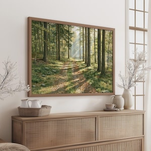 Puede incluir: Una impresión de arte mural de paisaje rectangular en un marco marrón que representa un sendero forestal con árboles altos, follaje verde y luz solar filtrándose a través del dosel. La escena muestra un camino de tierra con hojas caídas.