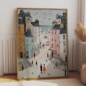 May include: A framed painting depicting a coastal town scene with multi-colored buildings in shades of yellow, blue, pink, and white. The street features several small figures, birds, and a view of the sea with sailboats in the background.