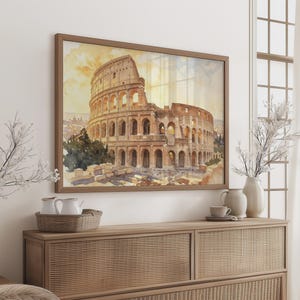 Puede incluir: Una lámina de arte mural rectangular con una acuarela del Coliseo de Roma en tonos amarillo dorado, marrón y crema. La obra está enmarcada en un marco fino de madera de tono medio y se muestra sobre una pared de color claro.