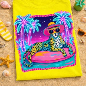 May include: A bright yellow t-shirt featuring a graphic of a leopard wearing a pink sun hat and sunglasses, lounging on a pink inflatable pool float. The design includes neon-style palm trees, a purple night sky, and a pink leopard print border.