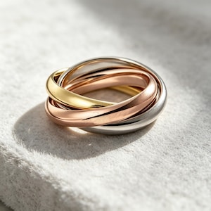 Può includere: Un anello tricolore composto da tre fasce intrecciate in oro giallo, oro rosa e metallo color argento lucido. Le fasce lisce e arrotondate sono intrecciate per formare un unico pezzo circolare con una finitura metallica riflettente.
