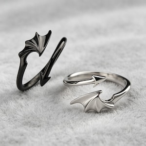 May include: Two open-style rings, one in a polished black finish and one in a polished silver-tone finish. Each ring features a design with a pointed arrow-shaped end and a stylized wing-shaped end, creating a wrap-around effect on the finger.