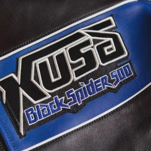 May include: A black and blue leather jacket featuring an embroidered patch with the text KUSO and Black Spider 500 in black, blue, and white thread. The garment includes white piping accents along the seams of the leather panels.
