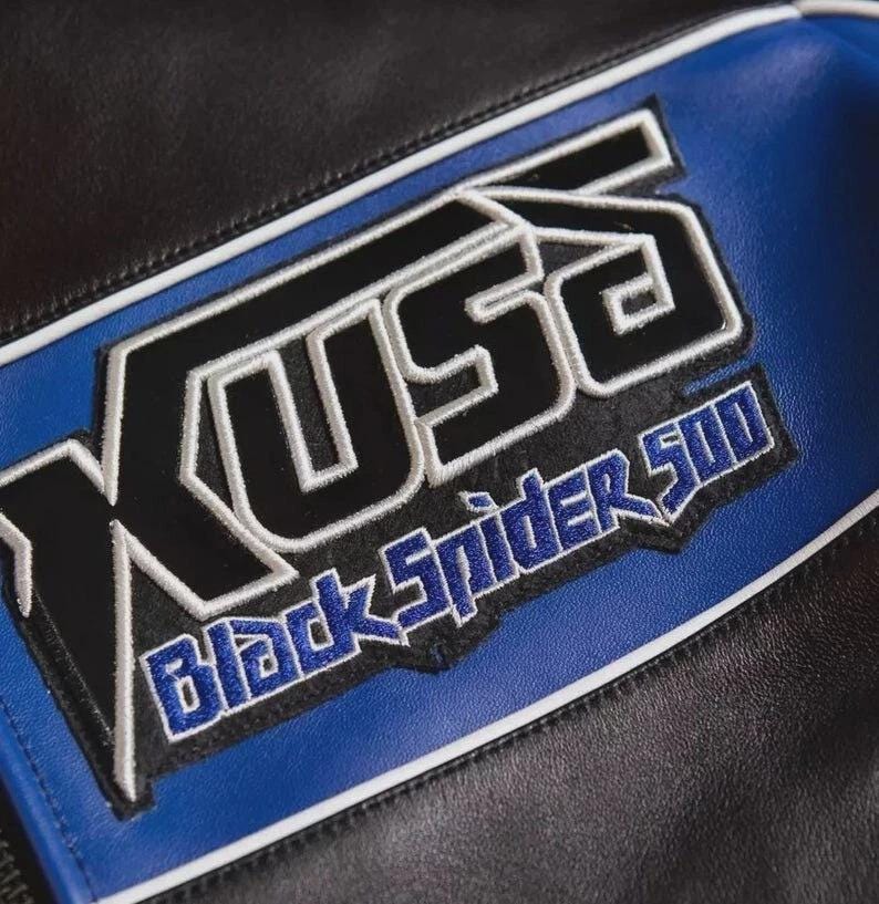 May include: A black and blue leather jacket featuring an embroidered patch with the text KUSO and Black Spider 500 in black, blue, and white thread. The garment includes white piping accents along the seams of the leather panels.