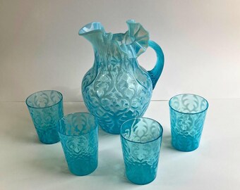 May include: A set of four blue glass tumblers and a matching pitcher with a ruffled rim and an embossed floral design.