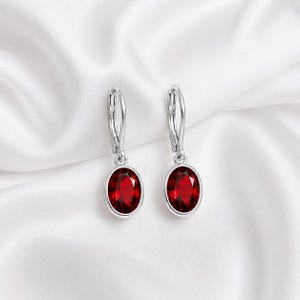 Peut inclure: Une paire de boucles d'oreilles pendantes argentées avec des pierres précieuses rouge foncé de forme ovale à facettes, serties dans des chatons en métal lisse. Elles sont dotées de fermoirs à levier sécurisés et d'une finition polie.