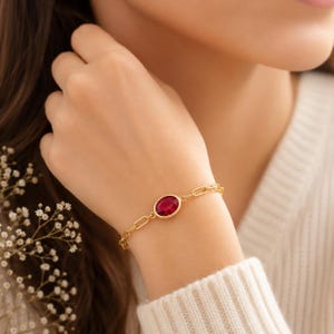 Peut inclure: Un bracelet à chaîne en or doté d'une pierre précieuse ovale rouge foncé sertie dans une monture en or lisse. Le bracelet est composé de maillons rectangulaires allongés en or qui se connectent au sertissage central de la pierre.