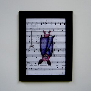 May include: A framed illustration of a purple bat hanging upside down from a music sheet. The bat has a pink face and is drawn in a cartoon style. The music sheet has musical notes and lyrics, including the words "the land of an ud-ed sky" and "a home where no storm clouds rise".