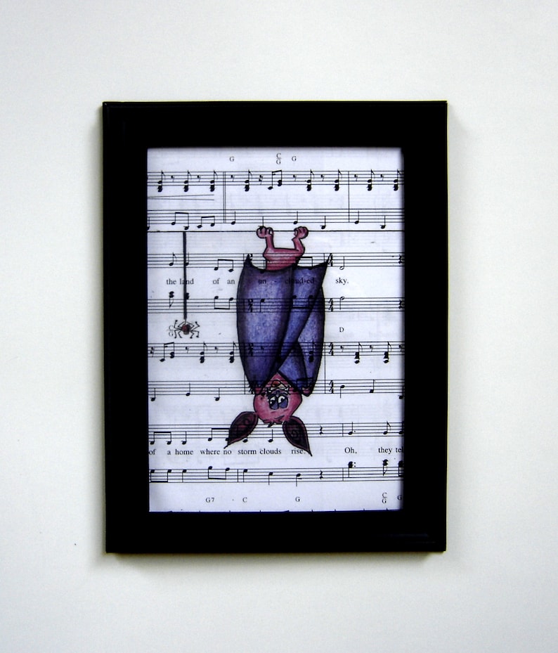 May include: A framed illustration of a purple bat hanging upside down from sheet music. The bat has a pink face and is smiling. The sheet music has the words "the land of an unclouded sky" and "a home where no storm clouds rise".