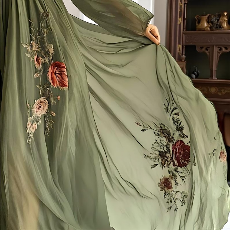 May include: Flowing olive green dress with long sleeves. The dress features intricate floral embroidery in shades of red, pink, and brown. The sheer fabric drapes elegantly, creating a soft, ethereal look. The floral design is concentrated on the bodice and hem.