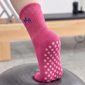 Op de afbeelding: Roze sportsokken met een antislip grip op de zool. De sokken hebben de initialen "Ms" geborduurd op de manchet. De sokken zijn ontworpen voor beweging en worden getoond op een grijze oefenbal.
