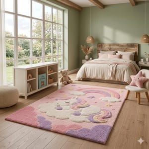 Può includere: Un tappeto rettangolare con un design trapuntato che raffigura un unicorno addormentato che riposa su una nuvola. Il tappeto presenta una tavolozza di colori pastello rosa, viola e giallo, con un arcobaleno, stelle e nuvole.