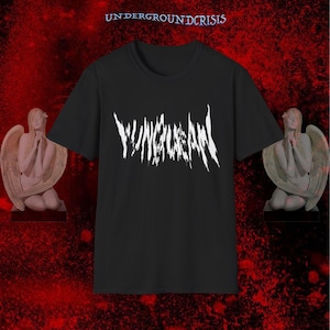 May include: Black t-shirt with the white text "YUNGLEAN" in a stylized font. The text is centered on the shirt. The words "UNDERGROUNDCRISIS" are at the top. Two angel statues are on either side of the shirt.