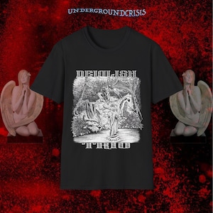 May include: Black t-shirt featuring a detailed black and white graphic of a forest scene with figures and the text "DEMILISH TRIO". The text "UNDERGROUNDCRISIS" is at the top. Two angel statues are on either side of the shirt.