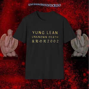 May include: A black short-sleeved t-shirt featuring yellow text that reads YUNG LEAN UNKNOWN DEATH and Japanese characters followed by 2002. The top of the shirt displays the text UNDERGROUNDCRISIS in a small, stylised font.
