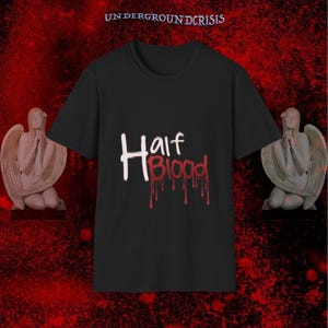 May include: Black t-shirt with the text "Half Blood" in white and red, with a dripping blood effect. The shirt is centered in the image, with angel statues on either side. The words "UNDERGROUNDCRISIS" are at the top.