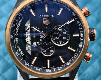 Könnte beinhalten: Eine TAG Heuer Carrera Calibre 1969 Chronographenuhr mit dunkelblauem Zifferblatt, bronzefarbener Lünette und schwarzem Lederarmband. Das Zifferblatt verfügt über drei Hilfszifferblätter, ein Datumsfenster und eine Tachymeterskala.