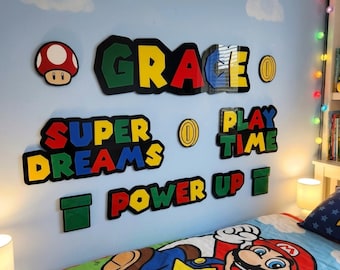 May include: Wall decor featuring a mushroom, coins, and phrases like "GRACE", "SUPER DREAMS", "PLAY TIME", and "POWER UP" in vibrant colors. The items are mounted on a light blue wall with cloud decals, creating a playful theme.