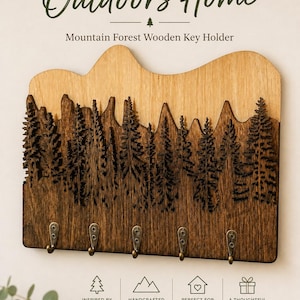 Könnte beinhalten: Ein Schlüsselhalter aus Holz mit einer geschichteten Berg- und Waldsilhouette. Der obere Teil ist aus hellem Holz, der untere Teil aus dunklem Holz mit fünf Metallhaken. Der Text lautet: Bring the Outdoors Home, Mountain Forest Wooden Key Holder.