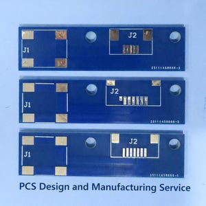 以下が含まれることがあります： J1とJ2のラベルが付いた、金色のコネクタを備えた3つの青い回路基板。各ボードには小さな穴と固有のシリアル番号があります。「PCS Design and Manufacturing Service」というテキストが下にあります。