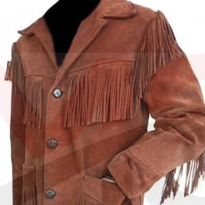 Peut inclure: Veste en daim marron avec des franges sur la poitrine, les manches et l'ourlet. La veste a une fermeture boutonnée, des revers crantés et deux poches avant. La veste est de couleur marron moyen.