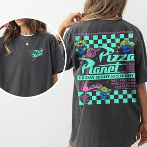 May include: Dark gray t-shirt with a Pizza Planet logo on the front and back. The back features the text "INTERSTELLAR FAST-FOOD FUELING STATION" and "FRIDAY NIGHT KID NIGHT" with alien characters and pizza graphics.