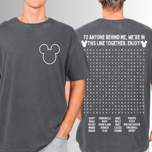 May include: Dark gray t-shirt featuring a white Mickey Mouse head on the front. The back of the shirt has the text "TO ANYONE BEHIND ME, WE'RE IN THIS LINE TOGETHER. ENJOY!" and a word search with Disney characters.