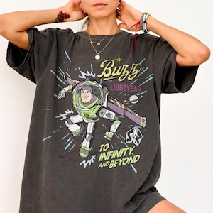 Puede incluir: Camiseta gris oscuro con un gr&aacute;fico de Buzz Lightyear en su traje espacial, con el texto "Buzz Lightyear" y "To Infinity and Beyond". El dise&ntilde;o incluye acentos verdes, morados y blancos.