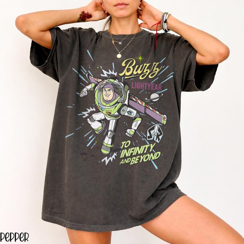 Puede incluir: Camiseta gris oscuro con un gr&aacute;fico de Buzz Lightyear en su traje espacial, con el texto "Buzz Lightyear" y "To Infinity and Beyond". El dise&ntilde;o incluye acentos verdes, morados y blancos.