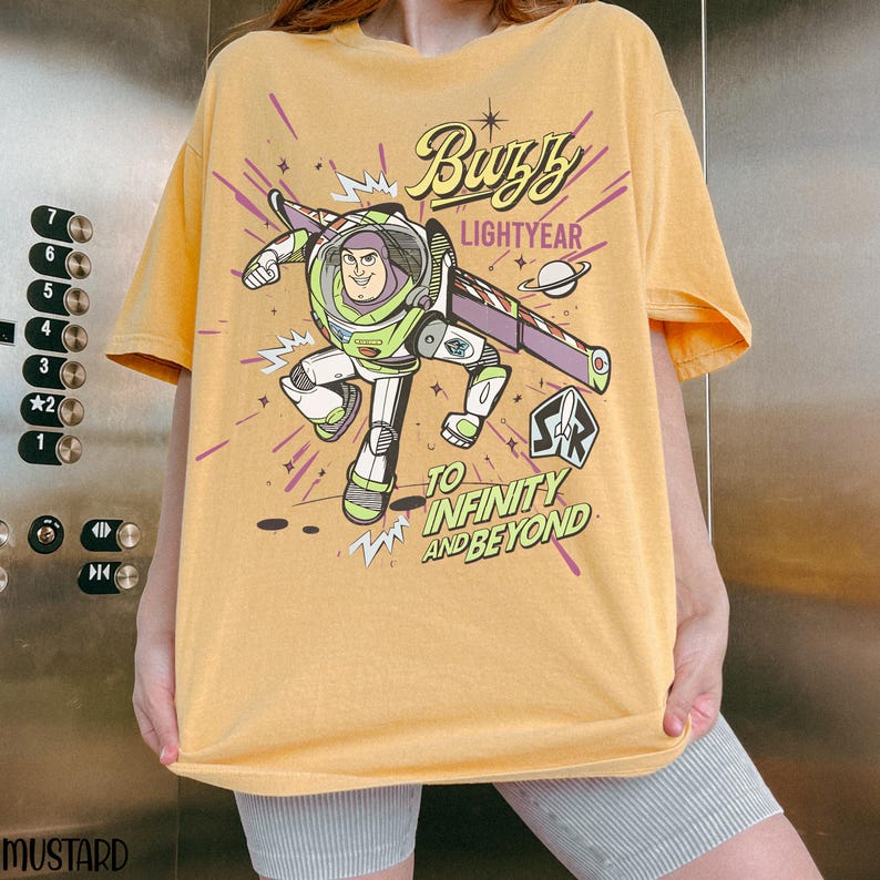 Puede incluir: Camiseta de color mostaza con un gr&aacute;fico de Buzz Lightyear, el texto "Buzz Lightyear" y "To Infinity and Beyond". El dise&ntilde;o incluye una imagen de dibujos animados de Buzz Lightyear con su traje espacial, con detalles en morado y amarillo.