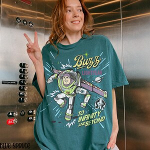Puede incluir: Camiseta de color verde azulado con un gr&aacute;fico de Buzz Lightyear, el texto "Buzz Lightyear" y "To Infinity and Beyond". El dise&ntilde;o incluye un tema espacial con un planeta y estrellas. Una prenda casual.