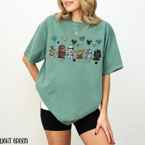 May include: Light green t-shirt featuring Star Wars characters holding balloons. The design includes BB-8, Chewbacca, a Stormtrooper, Grogu, R2-D2, and Darth Vader. The text "LIGHT GREEN" is at the bottom.