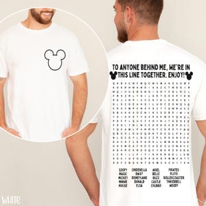 May include: White t-shirt featuring a black Mickey Mouse outline on the front. The back of the shirt has the text "TO ANYONE BEHIND ME, WE'RE IN THIS LINE TOGETHER. ENJOY!" with a word search puzzle and Disney character names.