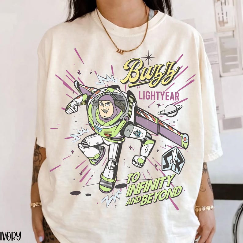 Puede incluir: Camiseta color marfil con un gr&aacute;fico de Buzz Lightyear en su traje espacial, con el texto "Buzz Lightyear" y "To Infinity and Beyond". El dise&ntilde;o incluye detalles en morado y blanco.