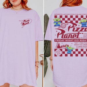 May include: A light purple t-shirt featuring the "Pizza Planet" logo on the front and a graphic on the back with the text "Interstellar Fast-Food Fueling Station." The back graphic includes the text "Friday Night Kid Night" and images of green aliens.