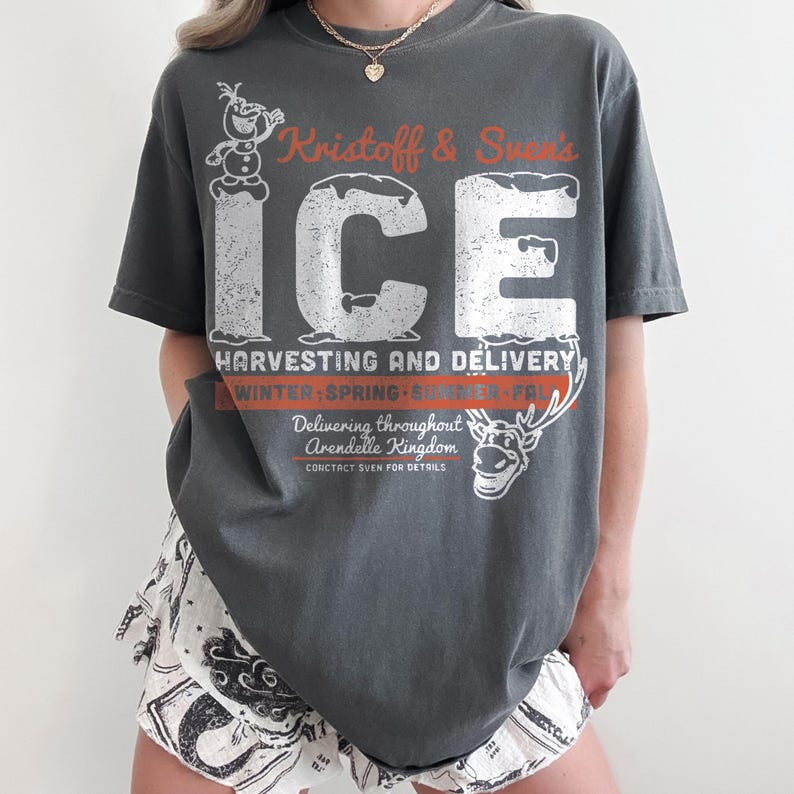 May include: Dark gray t-shirt with a distressed graphic featuring the text "Kristoff & Sven's ICE" and a snowman and reindeer illustration. The shirt also includes the text "Harvesting and Delivery" and "Delivering throughout Arendelle Kingdom."