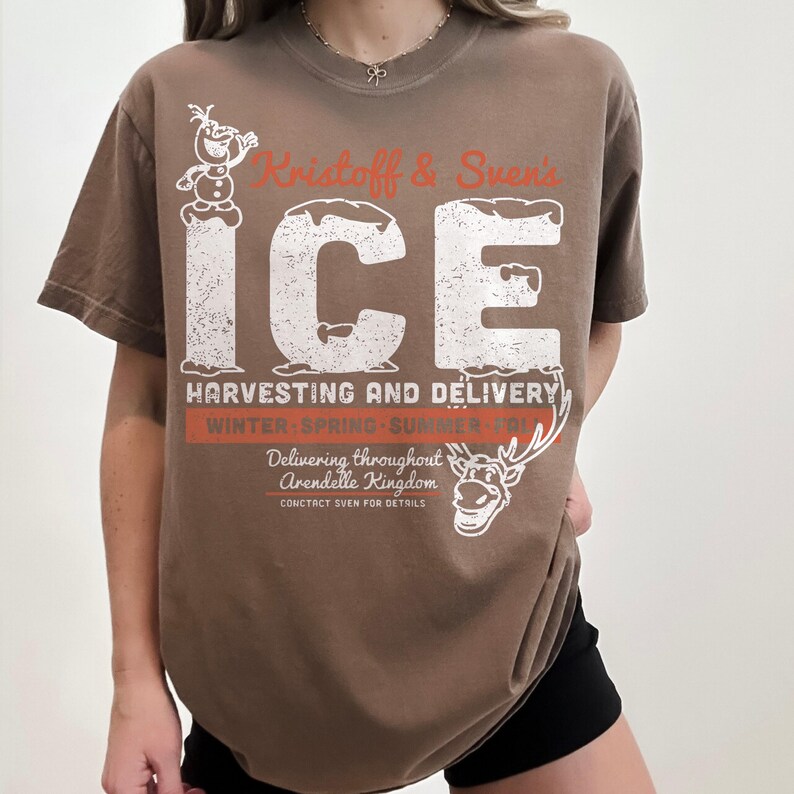 May include: Brown t-shirt featuring a distressed graphic with the text "Kristoff & Sven's ICE Harvesting and Delivery." The design includes images of Olaf and Sven from the movie Frozen. The shirt also has the text "Delivering throughout Arendelle Kingdom."