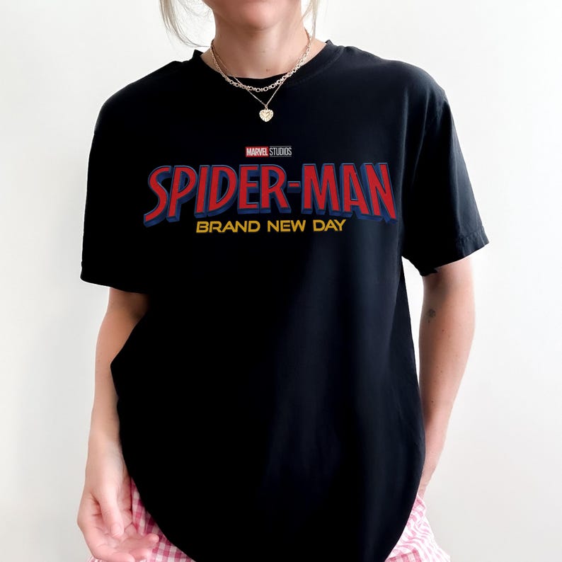May include: A black short-sleeved t-shirt featuring the Marvel Studios logo above the red and blue text Spider-Man and the yellow text Brand New Day printed on the chest. The shirt has a crew neckline and a standard fit for casual wear.